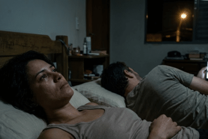 Fadiga emocional no casamento: mulher acordada e chorando na cama enquanto o marido está de costas mexendo no celular no escuro, ilustrando a distância de colegas de quarto.